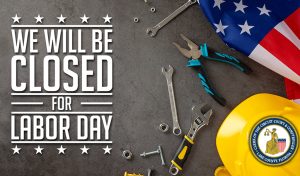 A variety of tools, nuts and bolts, an American Flag, and a hard hat lay on a concrete surface, and the words "We will be Closed for Labor Day."