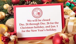 A Christmas tree surrounded by presents and ornaments, and a card that reads, "We will be closed Dec. 24 through Dec. 26 for the Christmas holiday, and Jan. 1 for the New Year's holiday."