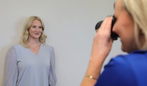 A woman stands against a wall as she gets her passport photo taken.